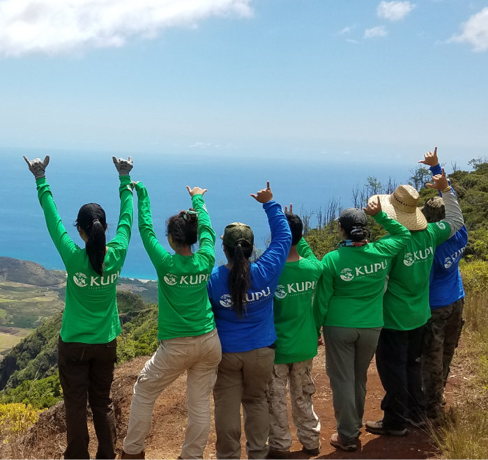 People in matching shirts celebrating on a scenic hillside overlooking the ocean.