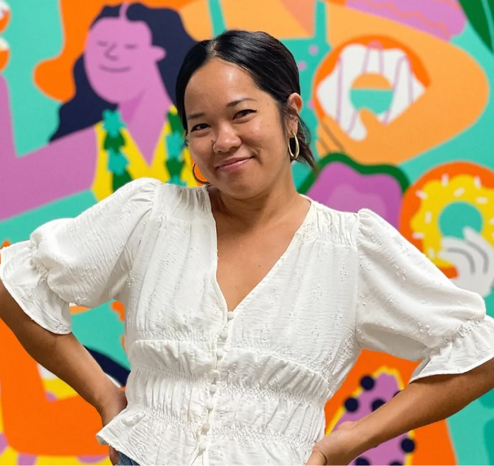 Person smiling in front of a colorful, abstract mural.