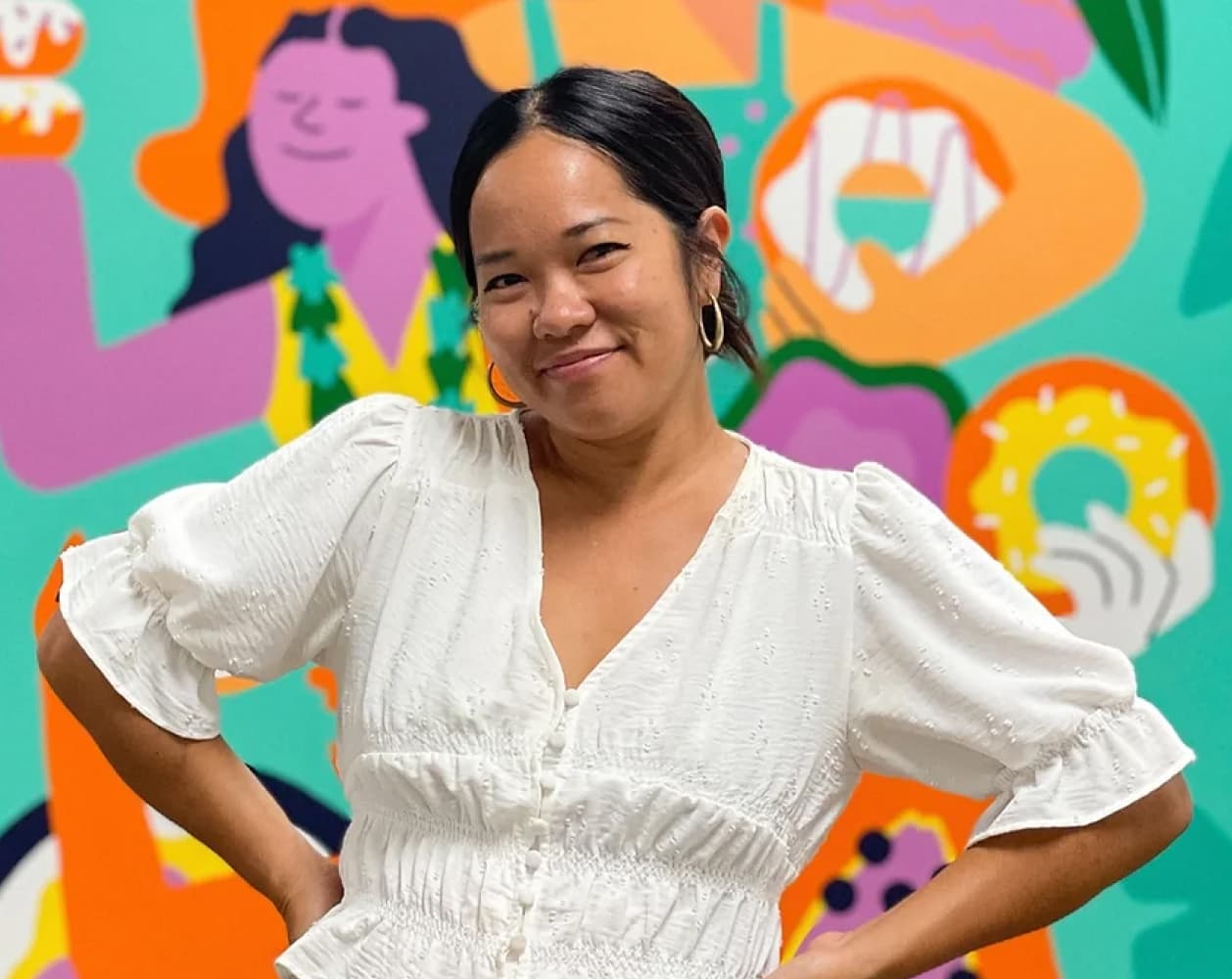 Person smiling in front of a colorful mural background.